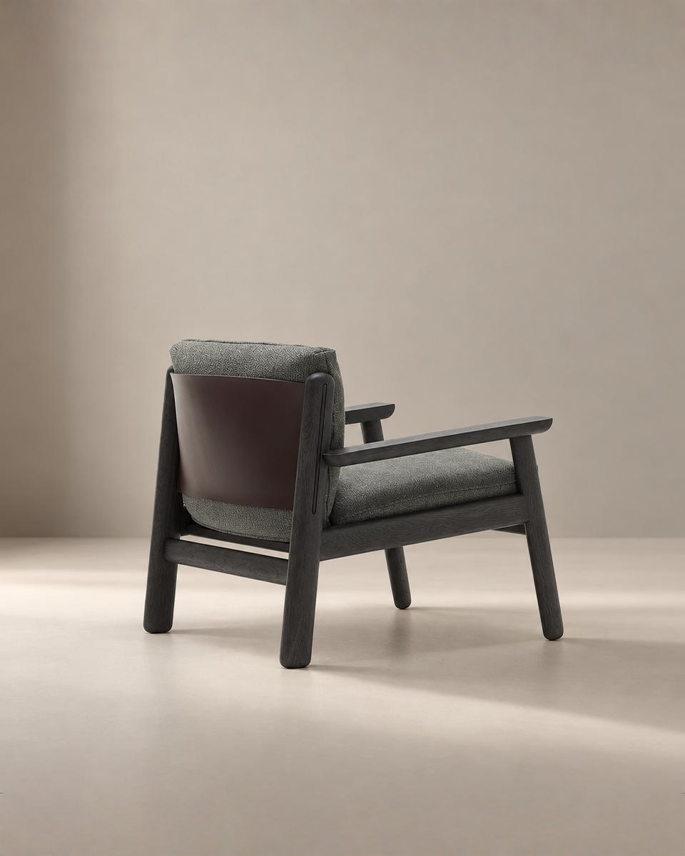A contemporary Wren Lounge Chair by Wooden Stories, featuring a solid walnut frame, gray fabric upholstered seat and backrest, and a brown leather accent on the reverse side, displayed against a plain beige background.