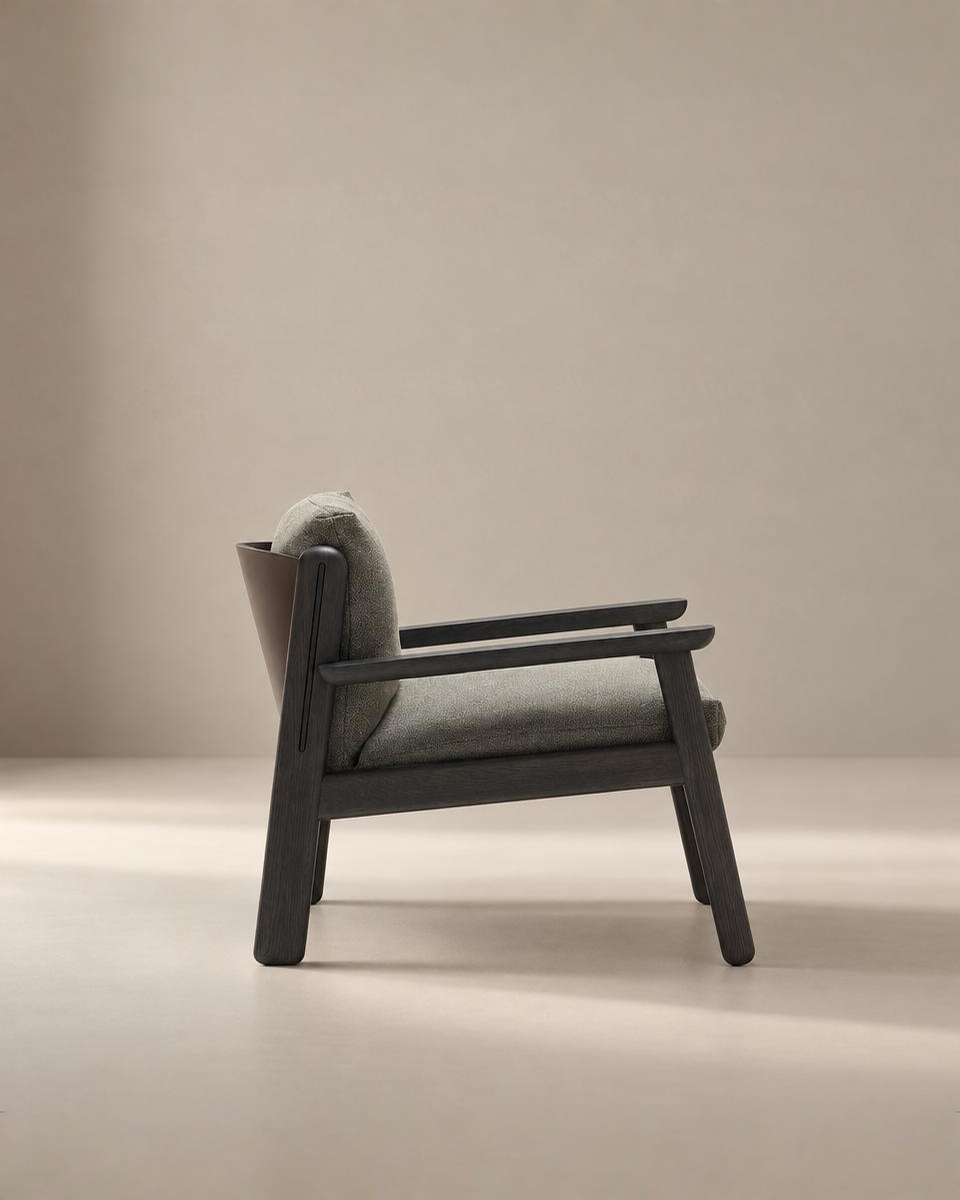 The Wren Lounge Chair | Fabric by Wooden Stories, featuring a solid walnut frame and gray upholstered seat and backrest, is photographed from the side against a plain beige background, evoking the timeless elegance of Danish design.