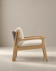 The Wren Lounge Chair | Fabric by Wooden Stories is displayed in side profile against a softly lit, neutral background. Crafted from solid walnut, this modern wooden armchair features beige upholstery, clean lines, and a minimalist, Scandinavian-inspired silhouette reminiscent of classic Danish design.