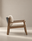 A modern wooden armchair—the Wren Lounge Chair | Fabric by Wooden Stories—crafted from solid walnut with light beige cushions and a black accent on the backrest, is placed on a light-colored floor against a plain beige background, embodying timeless Danish furniture design.