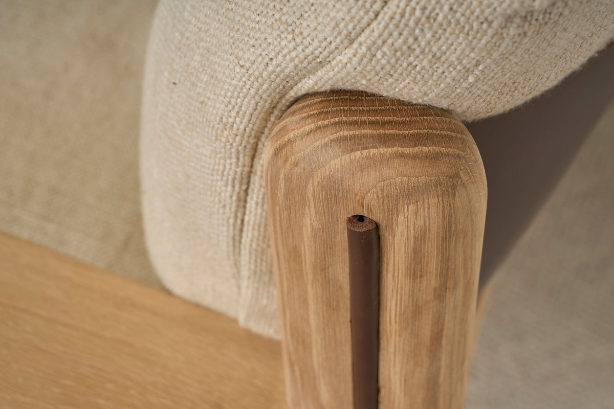 Close-up of the Wren Lounge Chair | Fabric by Wooden Stories, featuring a smooth solid walnut wood leg and a beige woven fabric cushion. The visible wood grain and soft upholstery showcase the materials and craftsmanship characteristic of Danish furniture design.