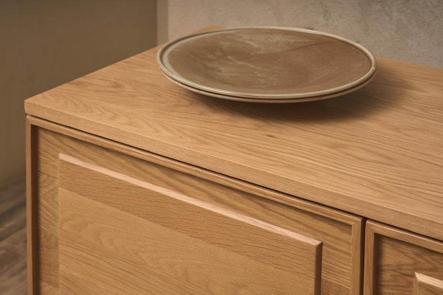 A close-up of the Yorke Sideboard by Wooden Stories, featuring clean Danish lines in light wood with a beige ceramic plate on top, set against a neutral wall.
