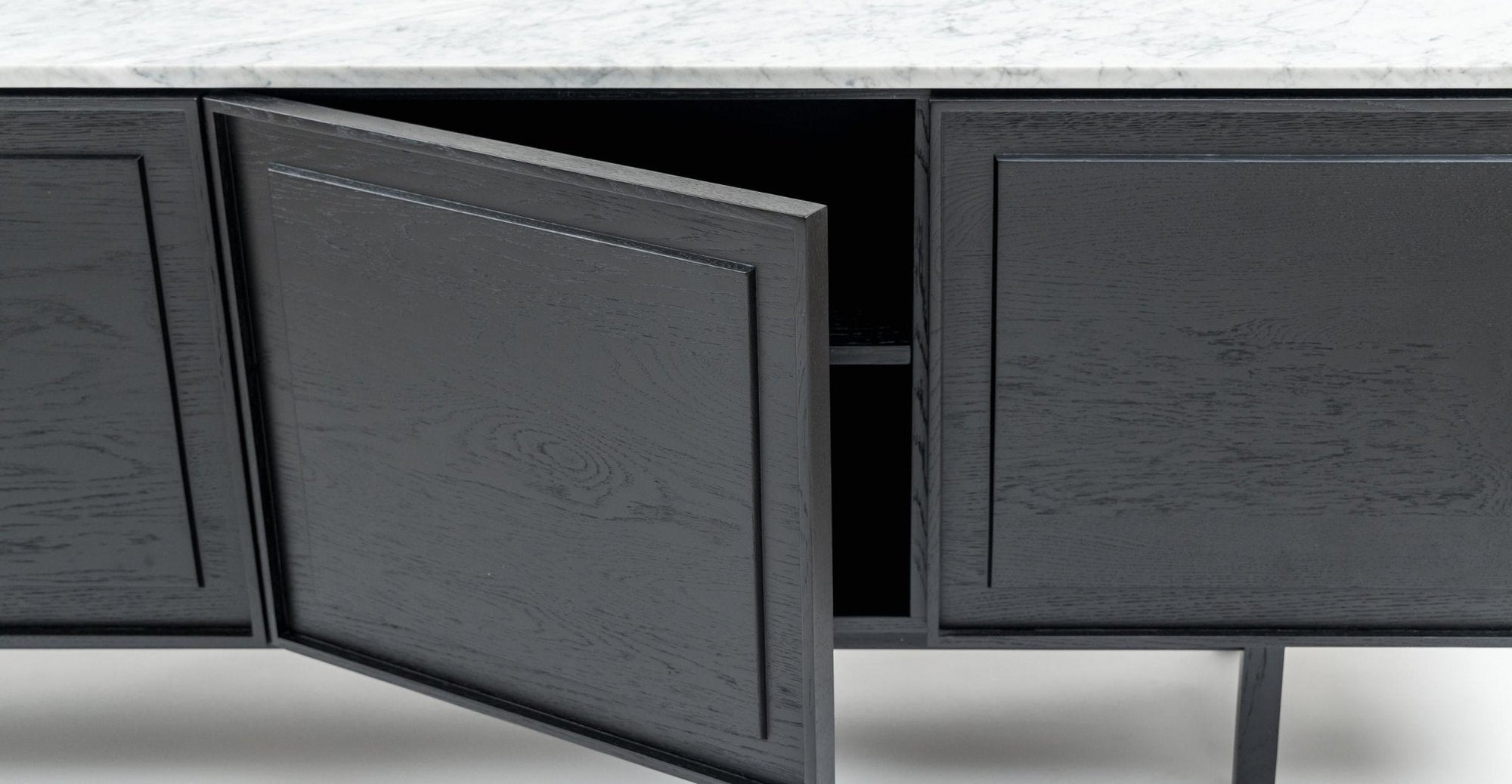A close-up of the Yorke Sideboard with Stone Top by Wooden Stories, featuring modern black wood, sleek Danish lines, and a white stone surface. One door is open, revealing an empty interior with a middle shelf.