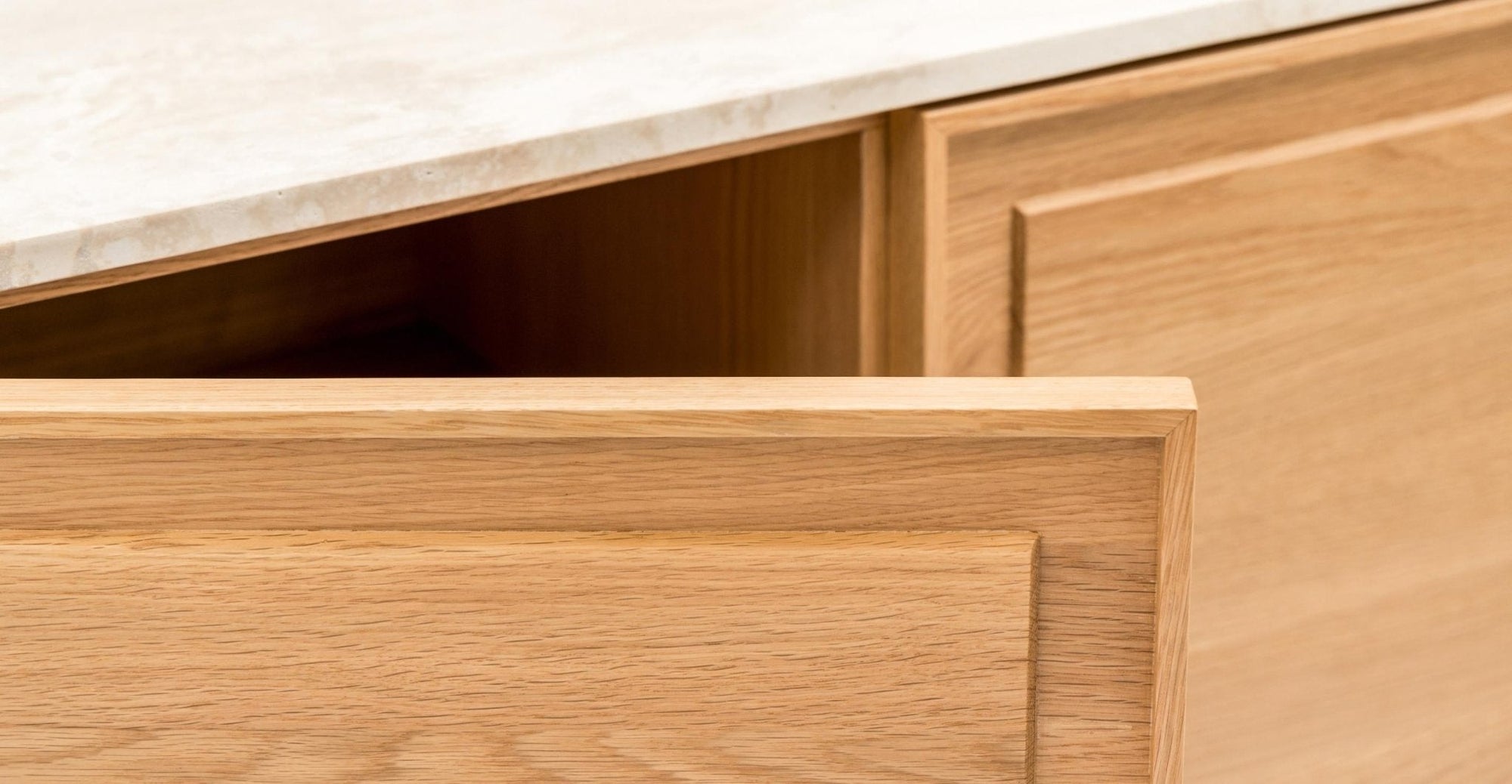 A close-up shows a wooden drawer partially open in the light-colored Wooden Stories Yorke Sideboard with Stone Top, beneath a light marble countertop, highlighting its subtle paneled motif.