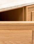 A close-up shows a wooden drawer partially open in the light-colored Wooden Stories Yorke Sideboard with Stone Top, beneath a light marble countertop, highlighting its subtle paneled motif.