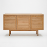 The Yorke Sideboard by Wooden Stories is a minimalist solid oak piece with three doors, a light natural finish, and Scandinavian design. It stands on four sturdy legs and is pictured against a plain white background.