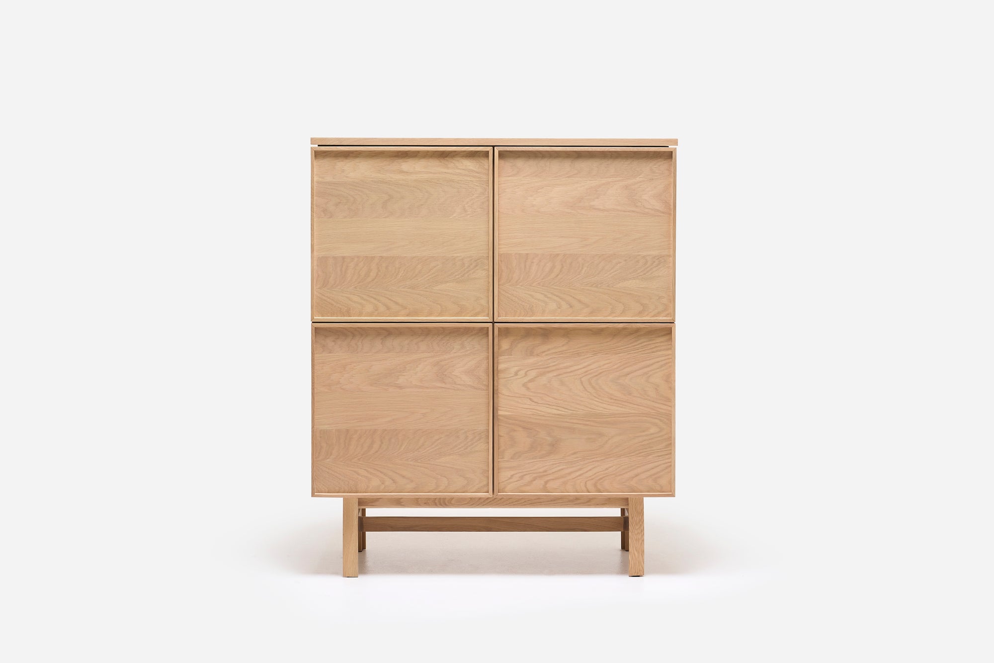 The Yorke Highboard by Wooden Stories features a minimalist, light wood design with four panel doors, clean lines, and stands on a matching wooden frame against a plain white background.