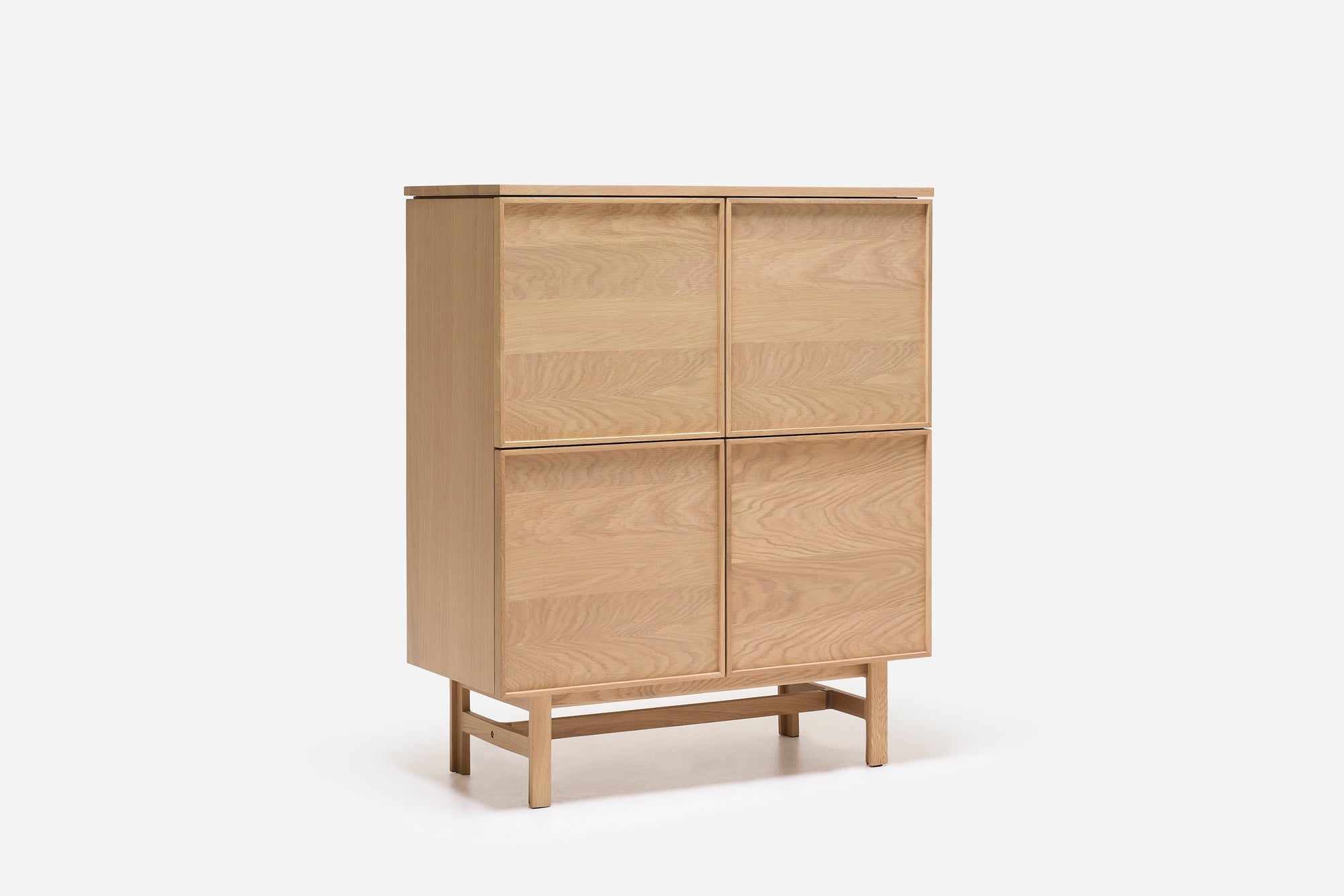 The Wooden Stories Yorke Highboard is a Scandinavian-inspired light wood cabinet with four square doors, a minimalist profile, and short legs connected by a horizontal support bar, shown against a plain white background.