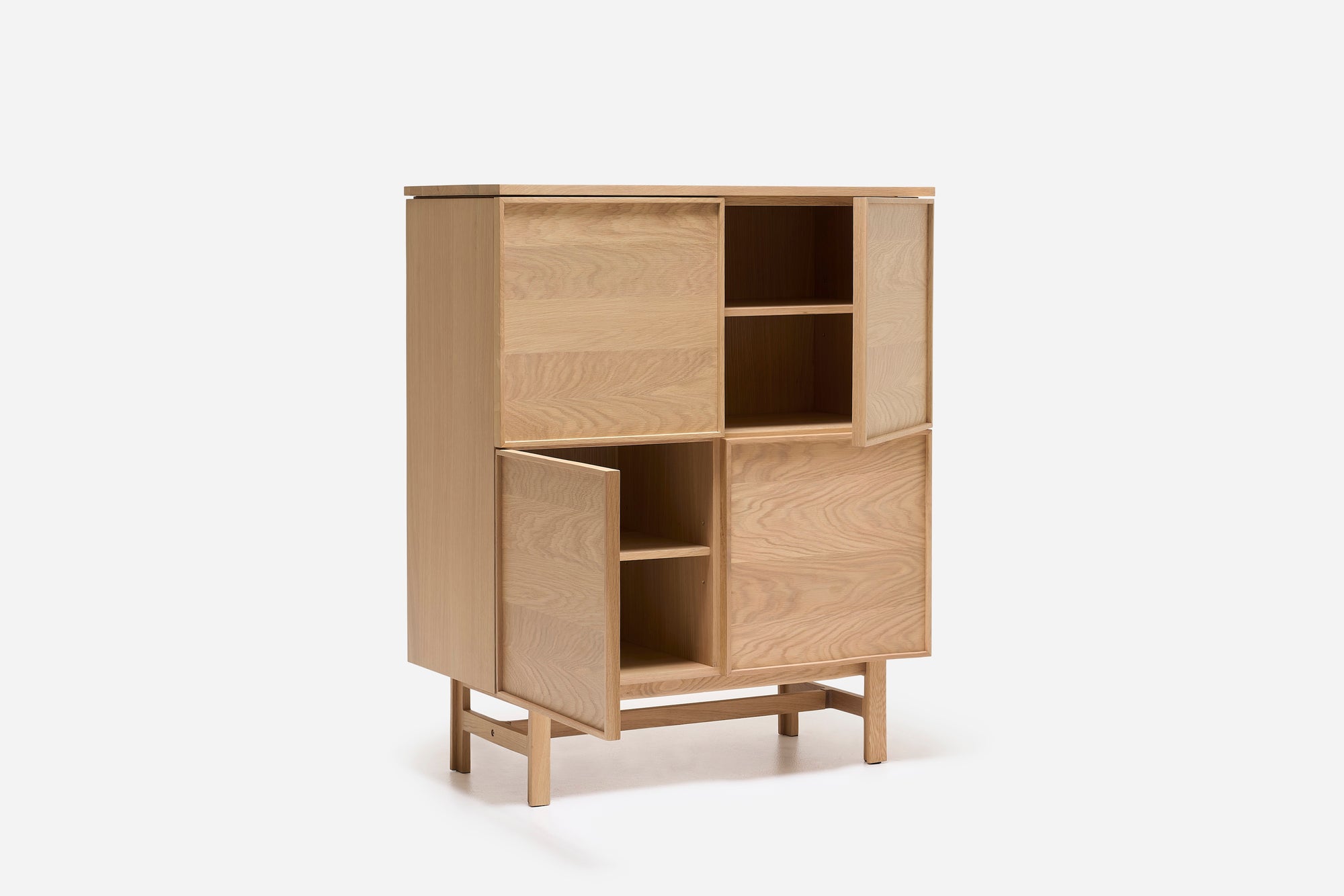 The Yorke Highboard by Wooden Stories is a light wood Danish cabinet with four compartments—two open shelves, two with partially open doors—and stands on four short legs with a crossbar, exemplifying classic Scandinavian design.