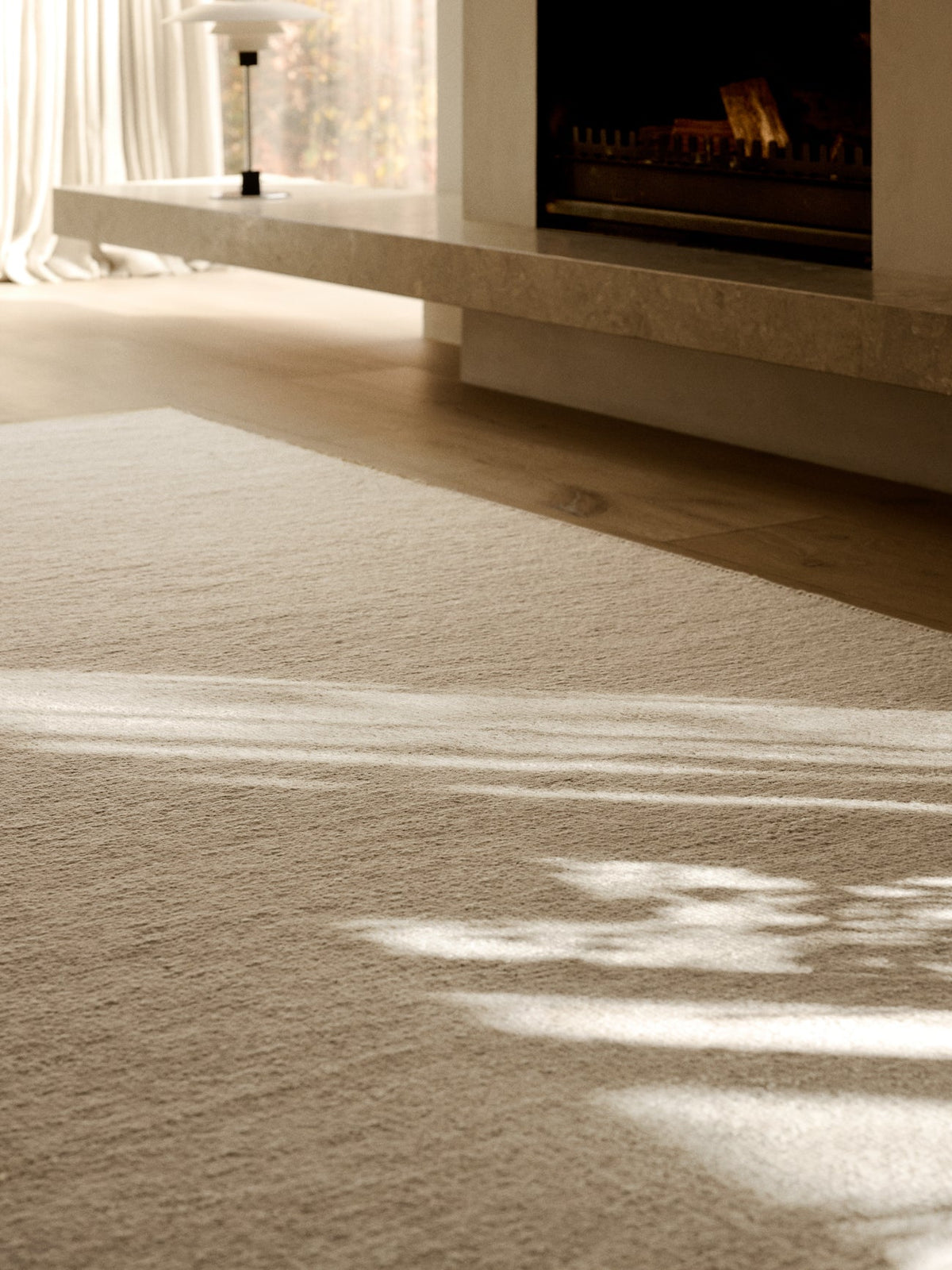 A textured, hand-knotted Aspen Rug - Sandstorm by Armadillo&Co covering a wooden floor in front of a fireplace.