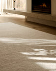 A textured, hand-knotted Aspen Rug - Sandstorm by Armadillo&Co covering a wooden floor in front of a fireplace.