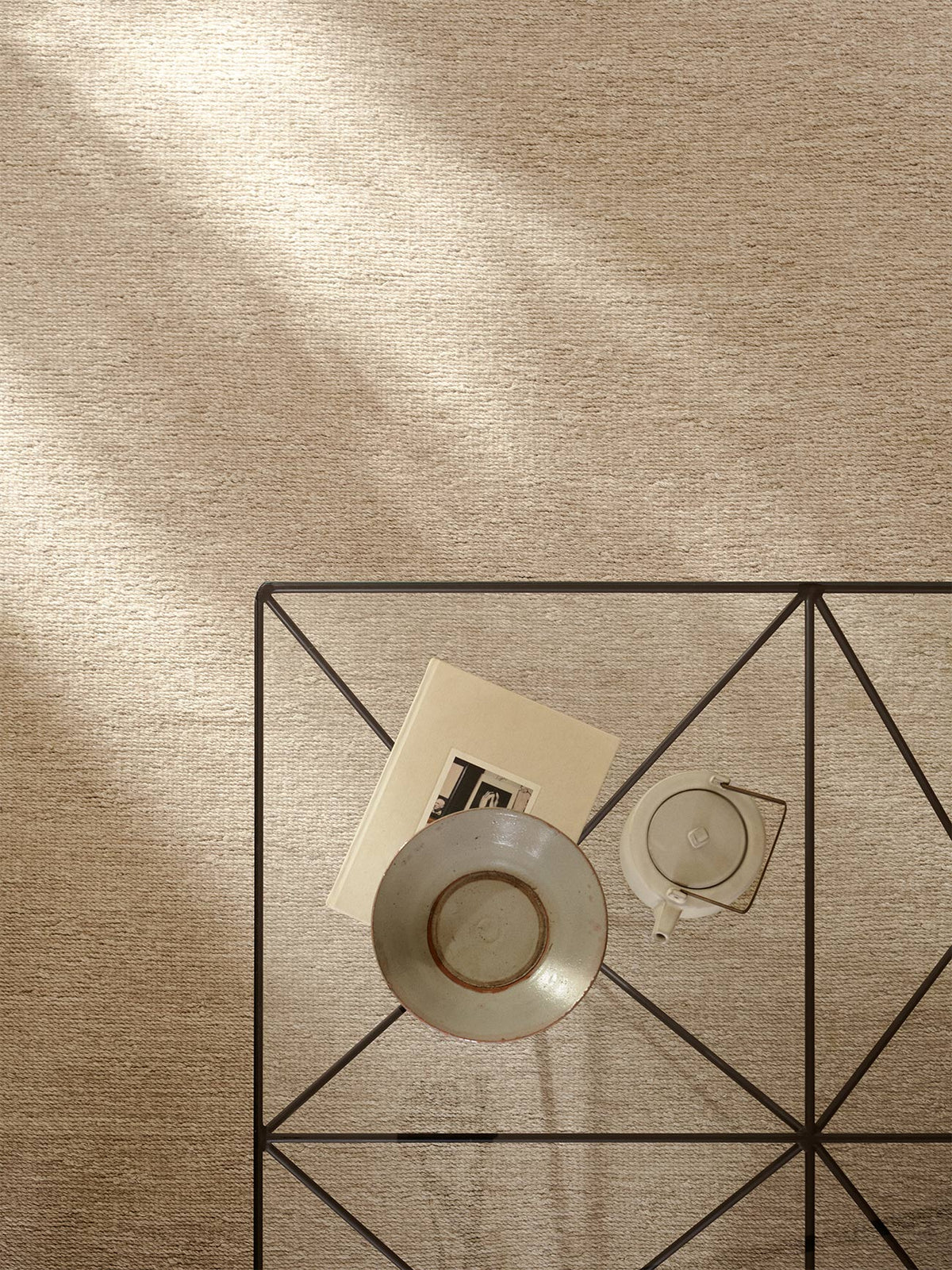 An overhead view of a tan, hand-knotted Armadillo&amp;Co Aspen Rug - Sandstorm, featuring a geometric metal side table topped with a book, a bowl, and a teapot.