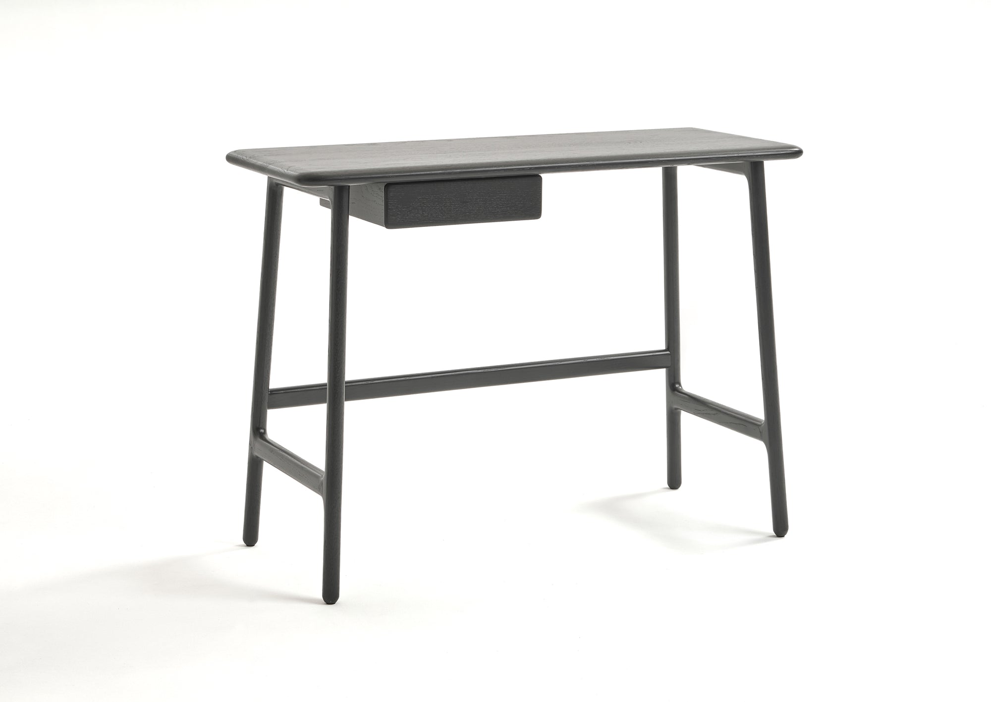 The Author Desk - Black Oak by Wooden Stories showcases four slender legs, a cork-lined central drawer, and a horizontal support bar—ideal for a minimalist home office against a crisp white background.
