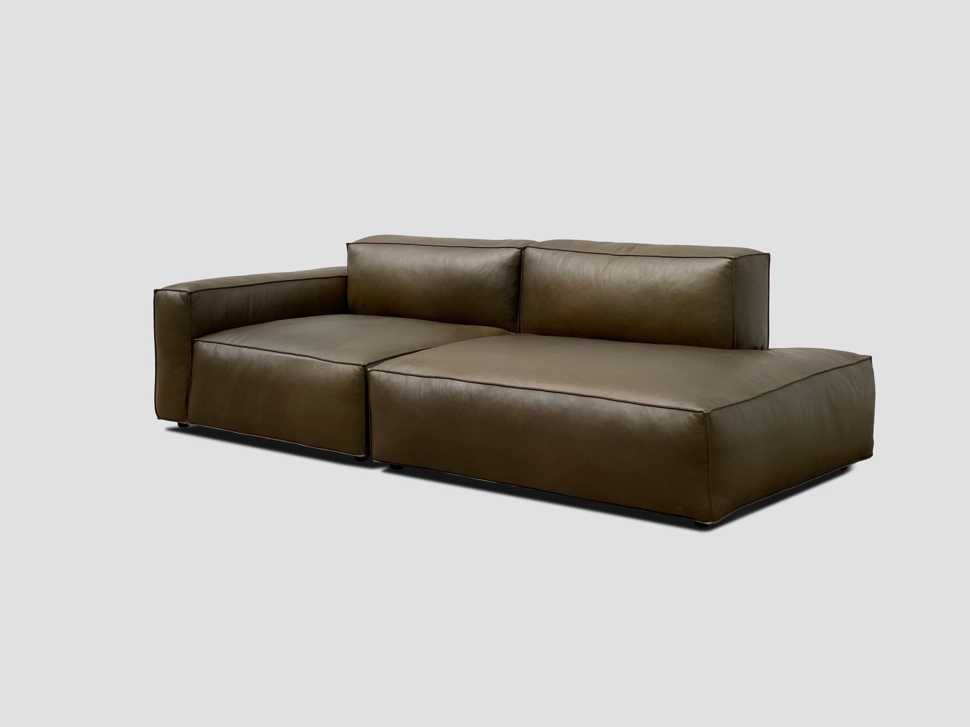 The Wooden Stories Baker Modular Sofa | Leather • M1 is a modern, dark brown leather sofa with a left-arm chaise, clean lines, and plush cushions, showcased against a plain light gray background.