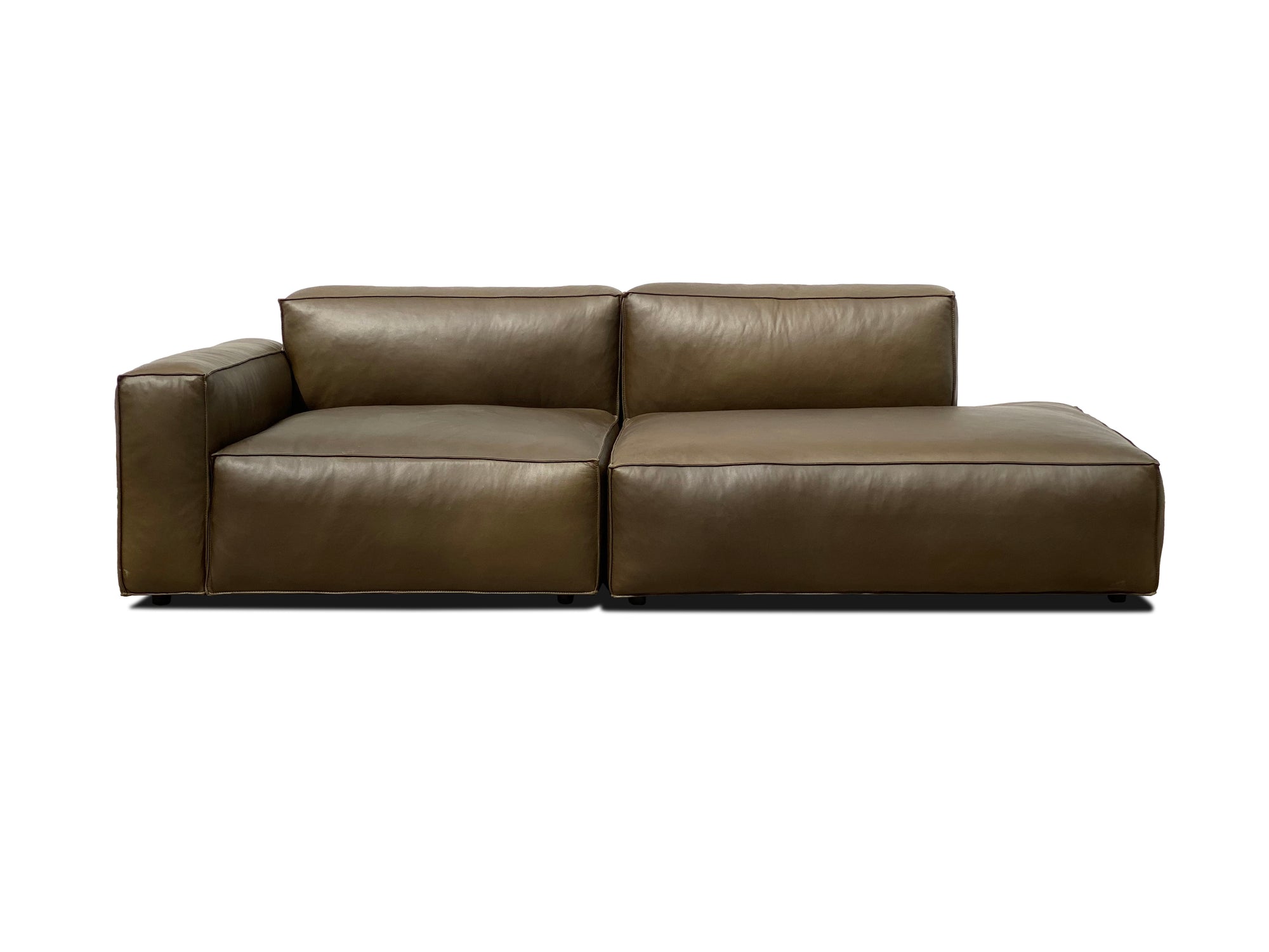 The Baker Modular Sofa | Leather • M1 by Wooden Stories is a modern, low-profile brown leather sofa with a left armrest and a wide right chaise, shown against a plain white background.