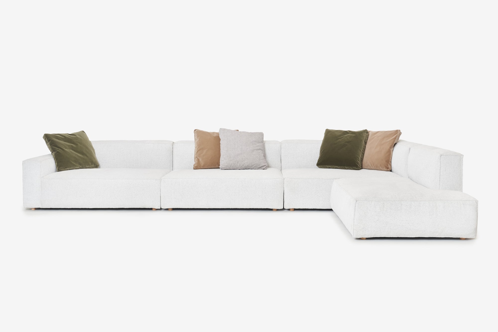 The Baker Modular Sofa | Fabric • M8 by Wooden Stories is a modern, white L-shaped sectional with five green, beige, and brown throw pillows, shown against a plain white background.