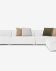 The Baker Modular Sofa | Fabric • M8 by Wooden Stories is a modern, white L-shaped sectional with five green, beige, and brown throw pillows, shown against a plain white background.