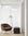 A modern minimalist room features the Ethnicraft Barrow Lounge Chair in Copper, a black floor lamp with a white shade, and a dark side table with books, set against sheer white curtains and light wood flooring for subtle vintage charm.