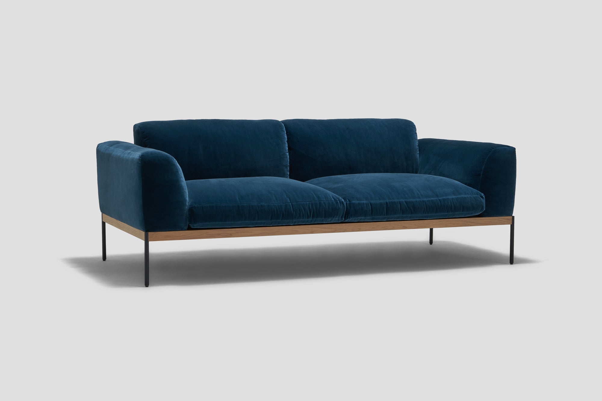 The Department Sofa 81&quot; by Wooden Stories showcases deep blue velvet fabric, plush cushions, Danish-inspired lines, upholstered panels, a solid wood plinth, and slim black metal legs, set against a plain light gray background.