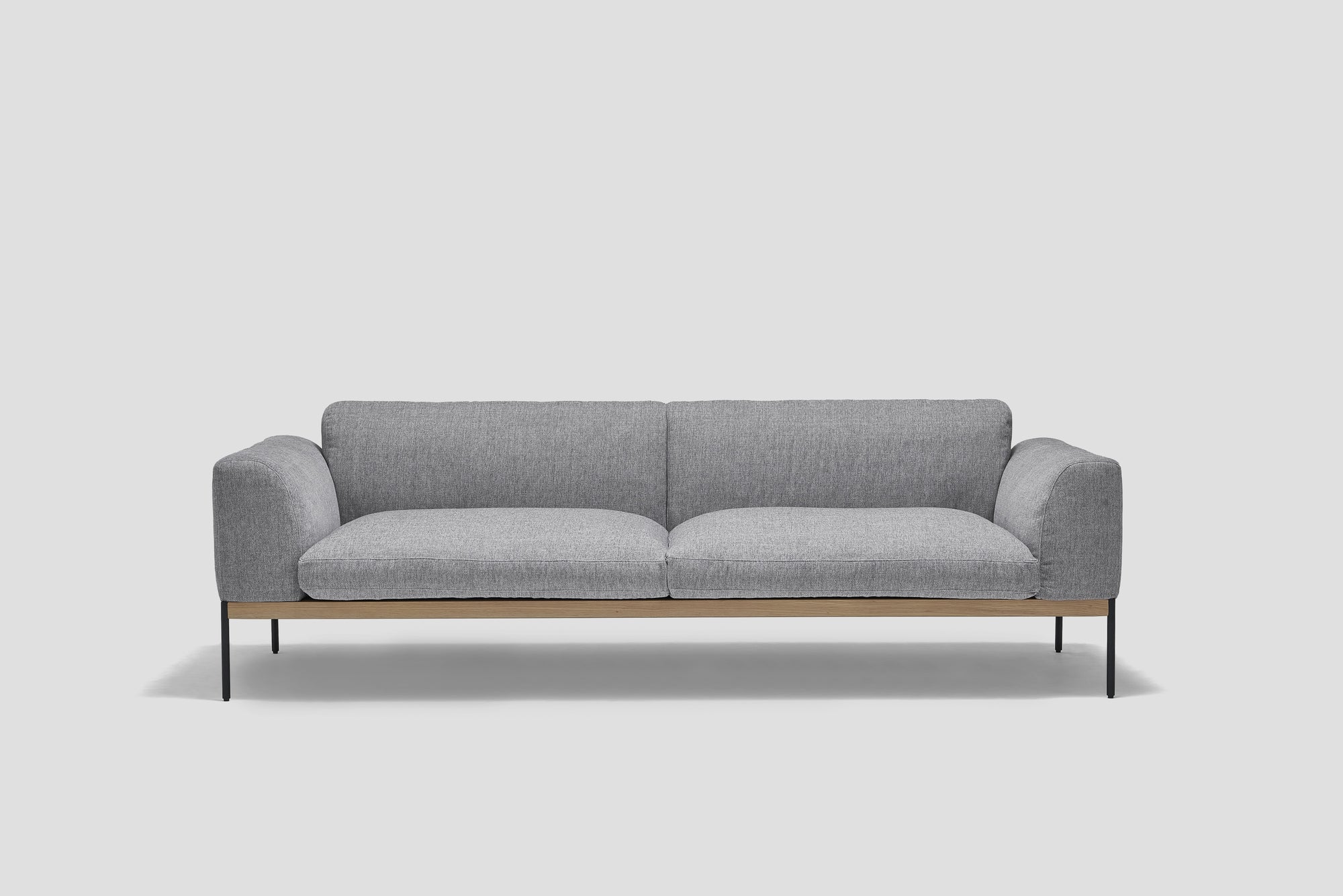 The Department Sofa 93&quot; by Wooden Stories features modern gray fabric, Danish lines, a solid wood plinth, slim black metal legs, wide armrests, and a minimalist design—ideal for both commercial and domestic crossover spaces.
