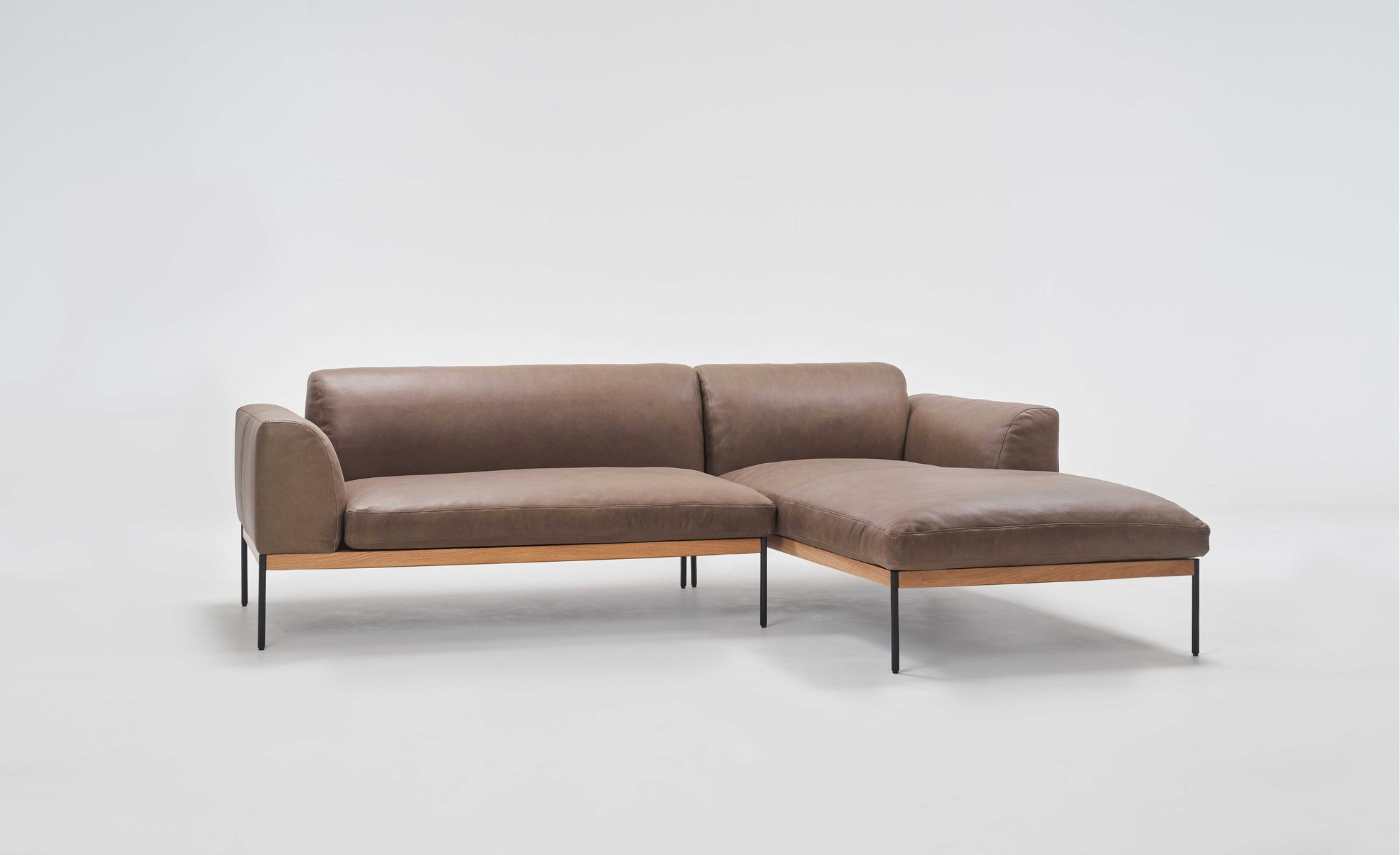 The Department Modular Sofa | Leather • M1 Right by Wooden Stories is a modern brown leather sectional with a right-side chaise, slim black metal legs, and a minimalist solid wood base, shown against a plain white background.