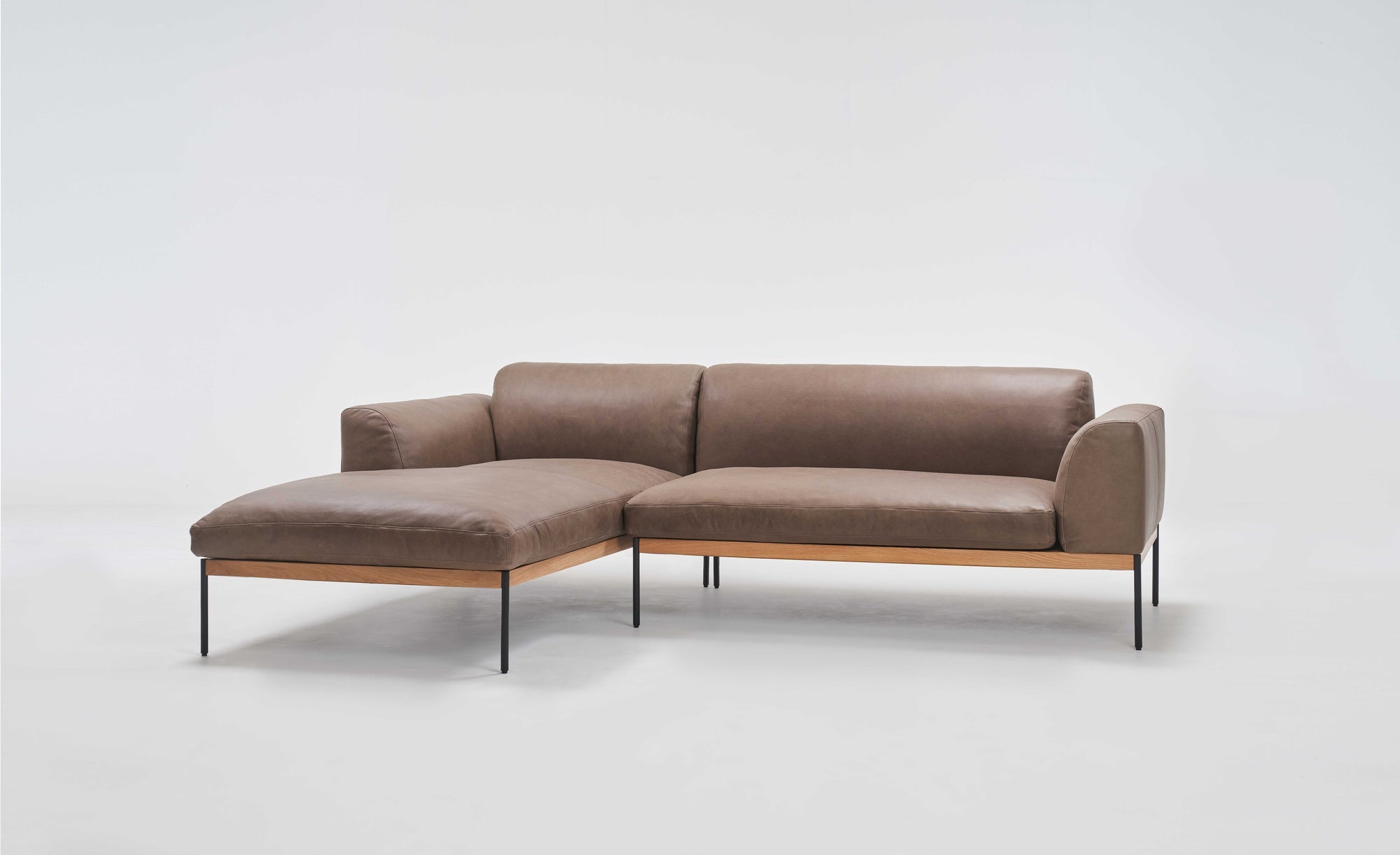 The Wooden Stories Department Modular Sofa | Leather • M1 Left features brown leather cushions, a left-side chaise, and slim black metal legs on an FSC-certified oak base, shown against a plain white background.