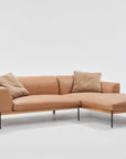 The Department Modular Sofa | Leather • M1 Right by Wooden Stories is a tan L-shaped sectional with slim black legs, solid wood base, two matching cushions, and a right-side chaise lounge, inspired by Danish design and shown on a plain white background.