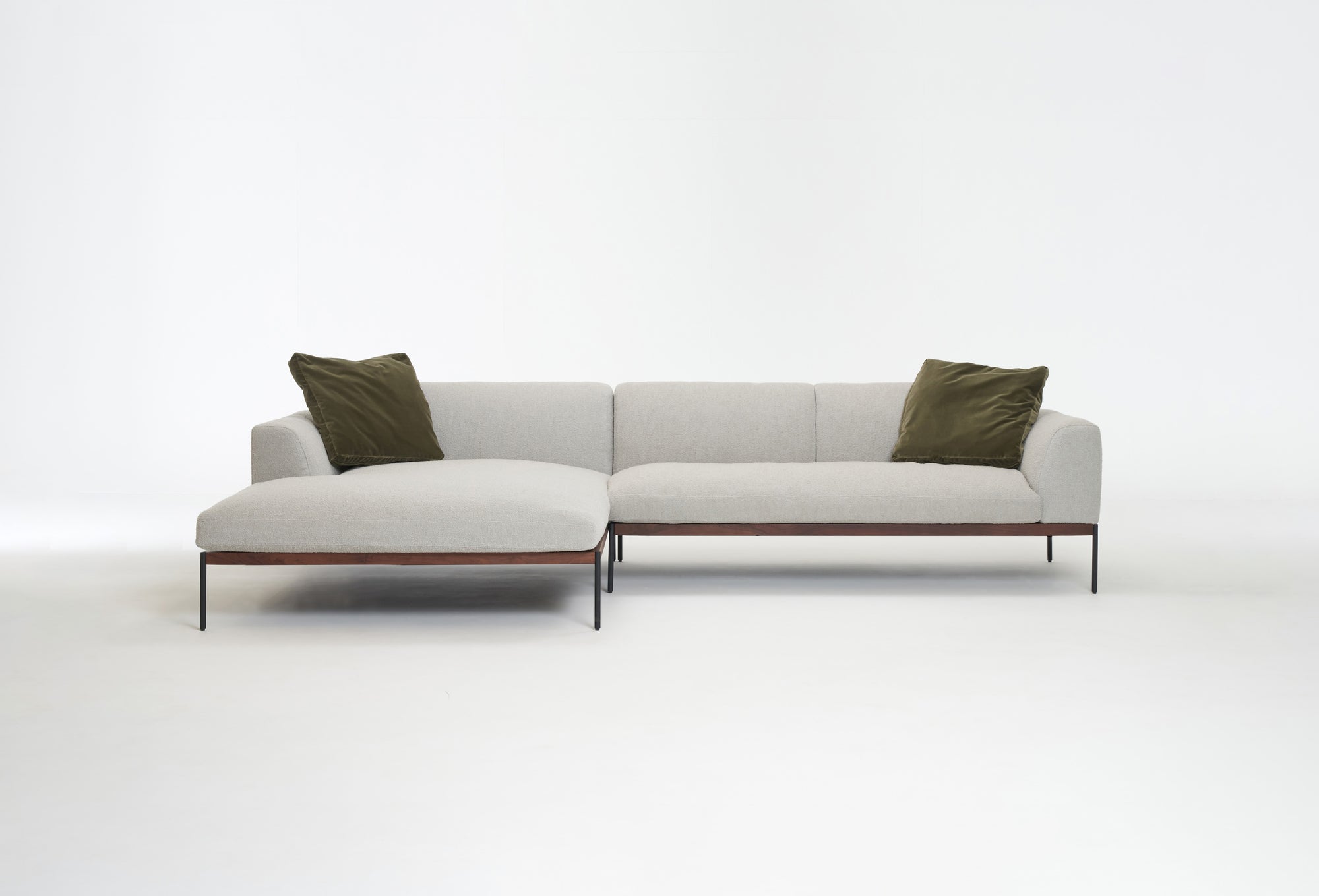 The Department Modular Sofa | Fabric • M4 Left by Wooden Stories features a modern light gray design with slim black legs, a solid wood base, and two olive green throw pillows, set against a plain white background.