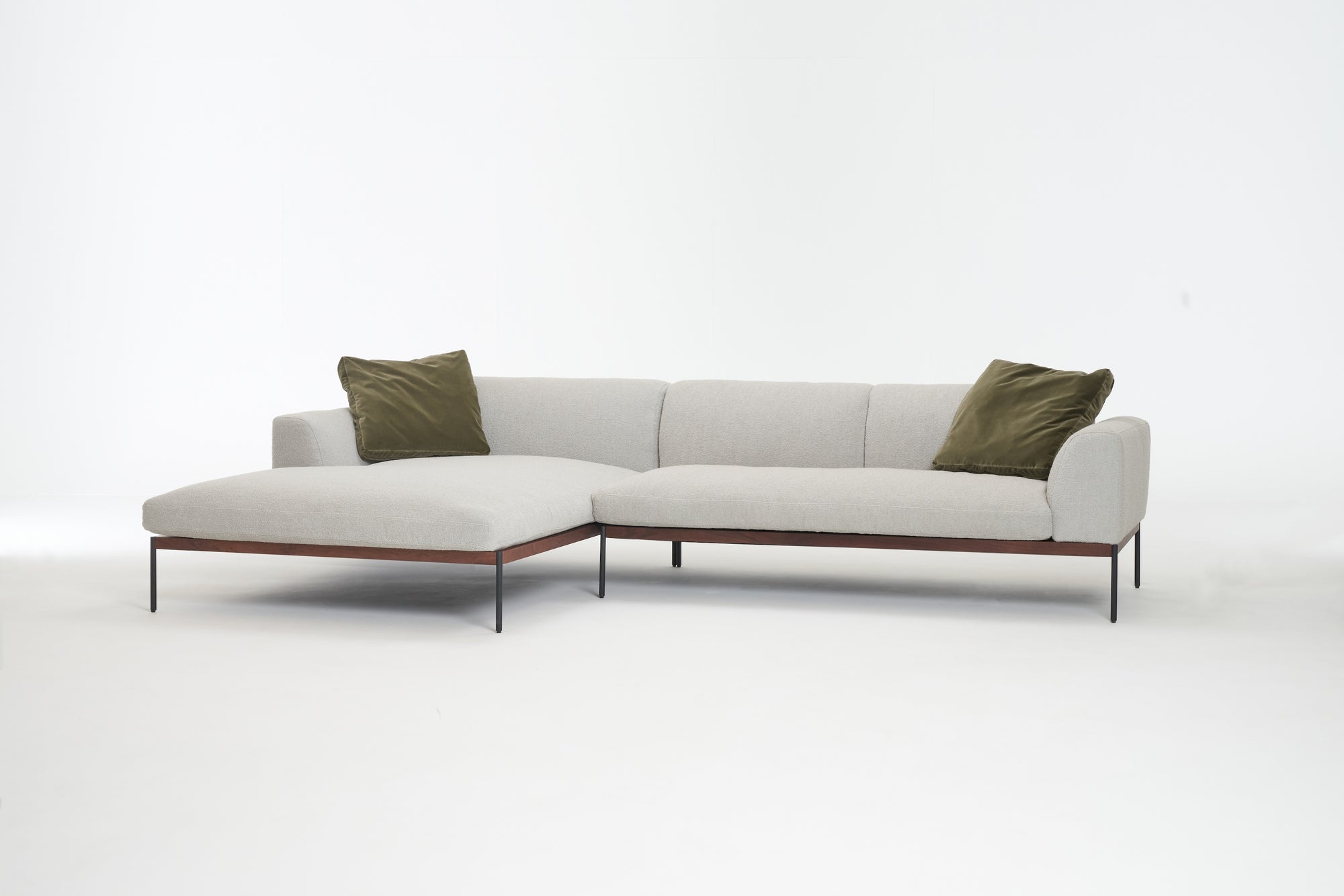 The Wooden Stories Department Modular Sofa | Fabric • M4 Left is a modern light gray sectional with slim black legs, an FSC-certified oak base, and two olive green throw pillows, shown against a plain white background.