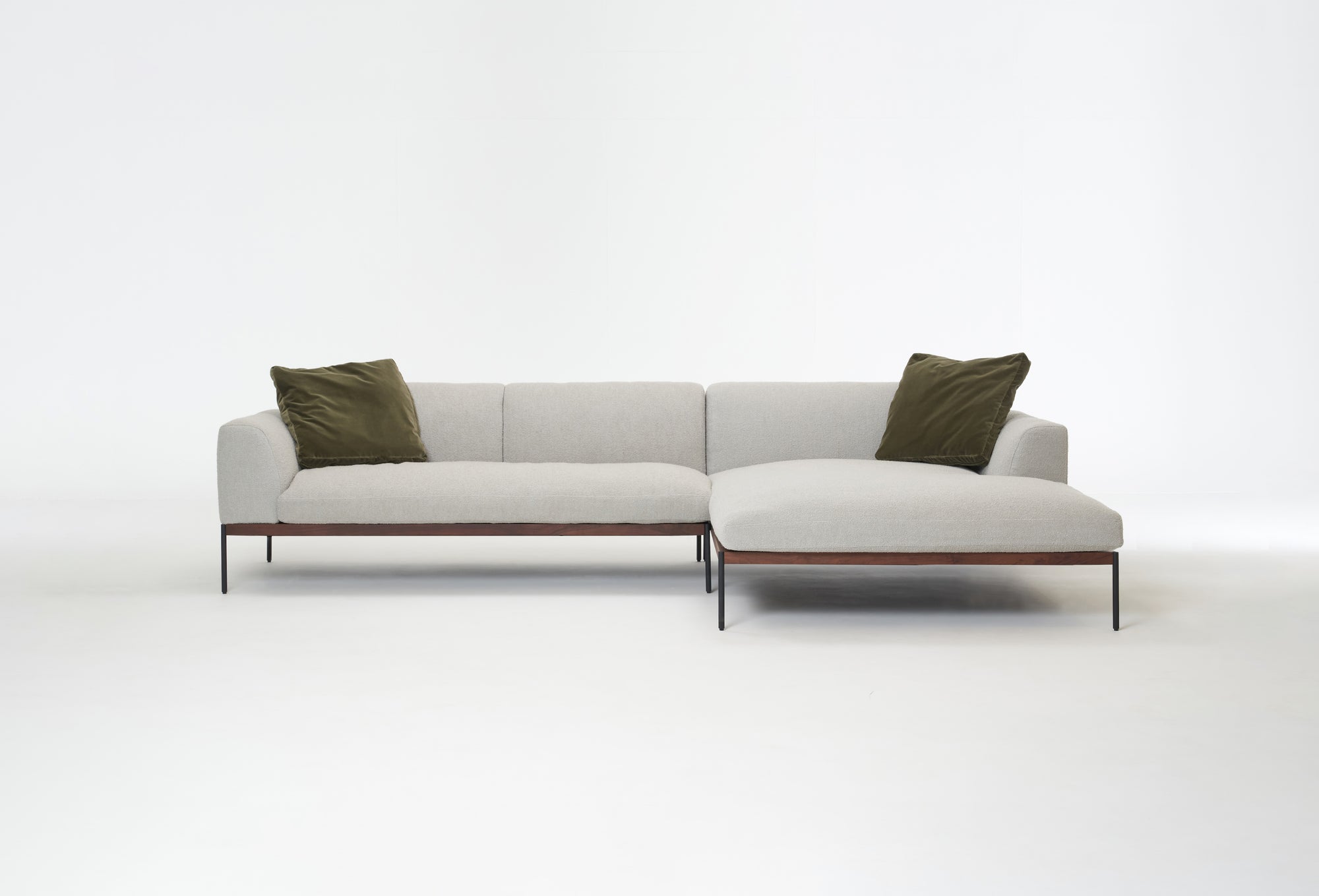 The Department Modular Sofa | Fabric • M4 Right by Wooden Stories is a modern, light gray L-shaped sectional with thin solid wood legs and two olive green square pillows, shown against a plain white background.