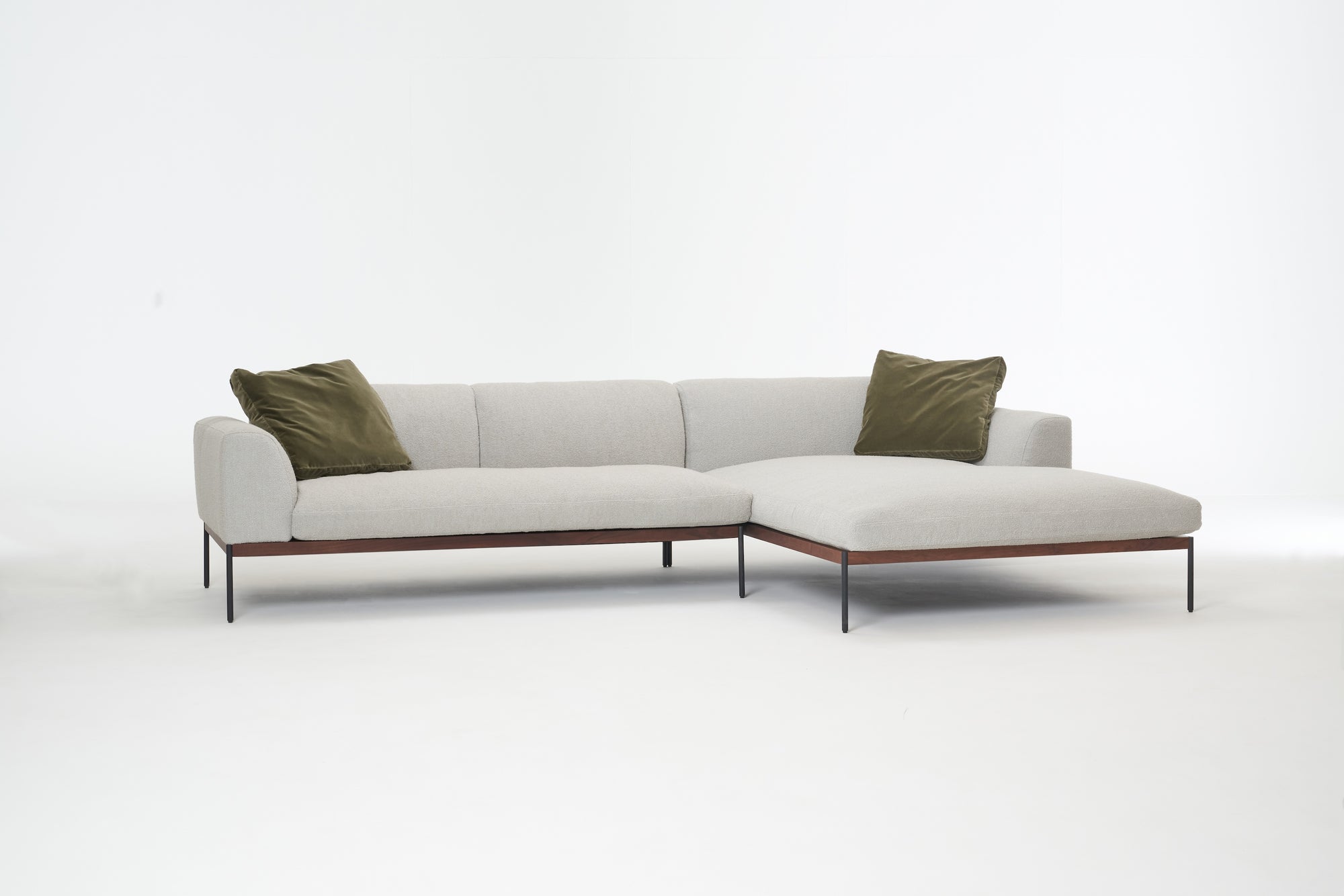 The Wooden Stories Department Modular Sofa | Fabric • M4 Right is a modern light gray sectional with a solid wood base, slender black legs, and two green throw pillows, shown against a plain white background.