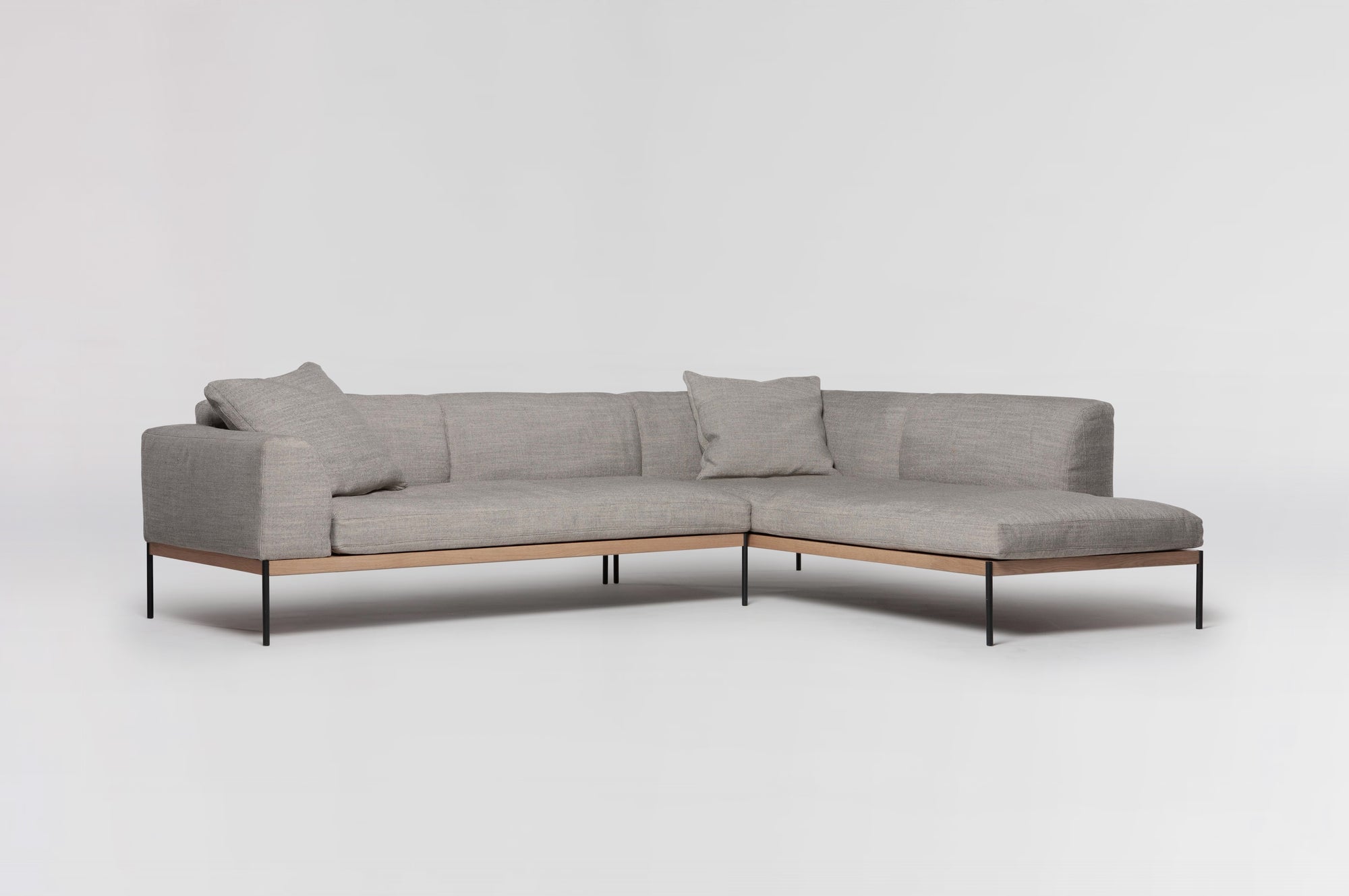 The Wooden Stories Department Modular Sofa | Fabric • M6 Right features light gray upholstery, slim black metal legs, FSC-certified oak trim at the base, and two matching cushions, shown against a plain white background.