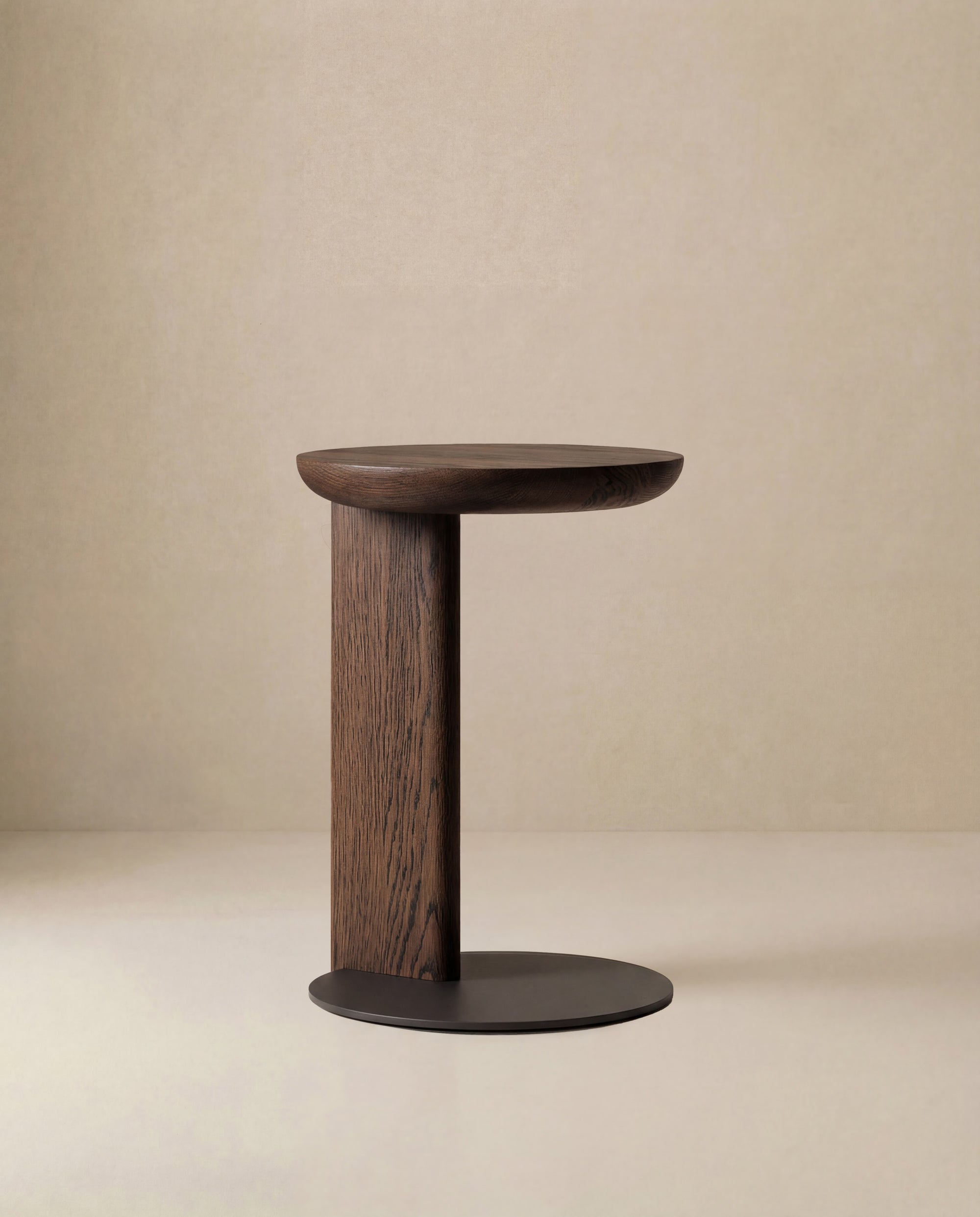 The Wooden Stories Guild Side Table features a modern, minimalist C-shaped design and a dark solid oak finish, shown against a plain beige background.