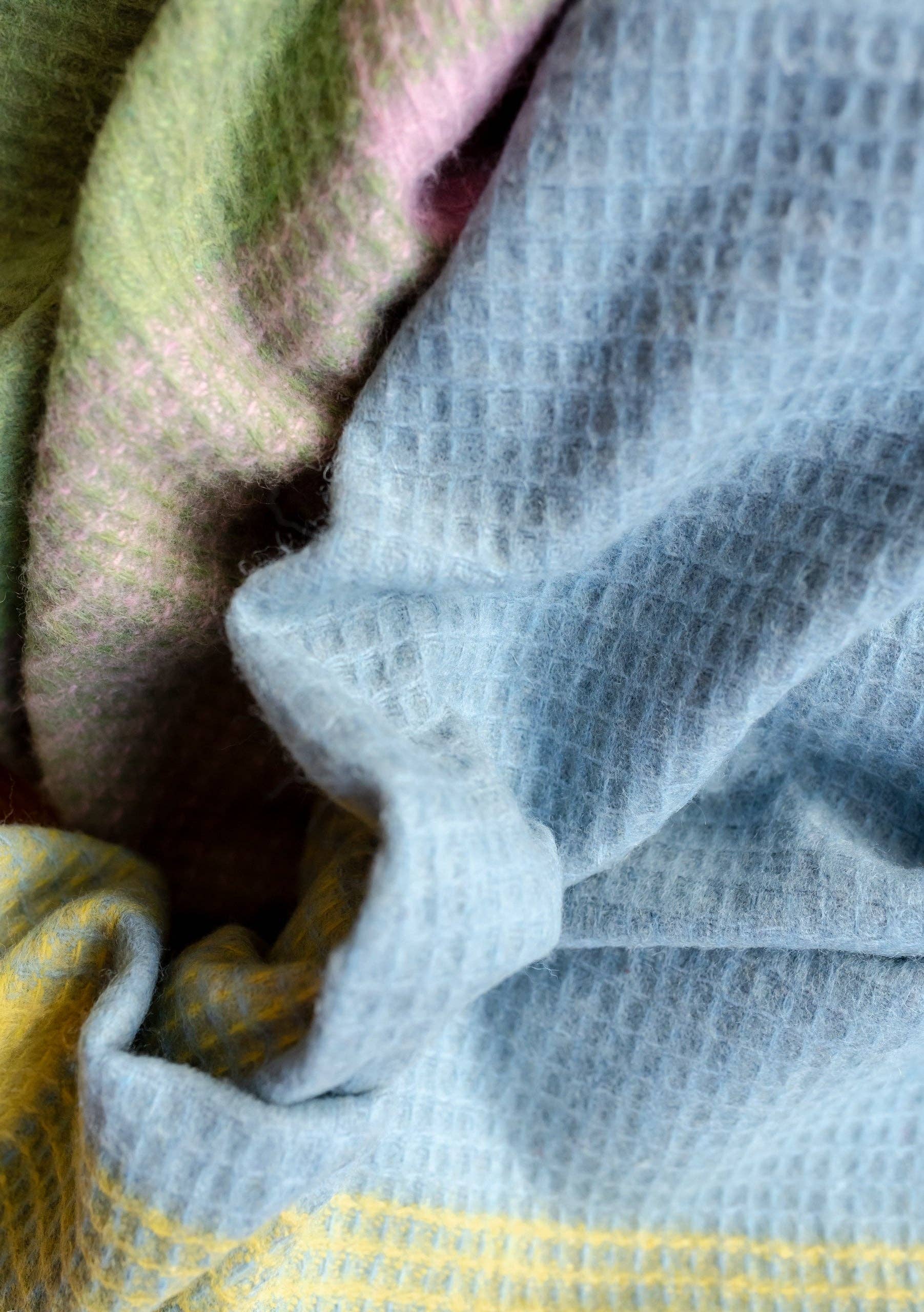 A close-up of FAIRE/TBCo’s Recycled Wool Blanket in Green Waffle Block highlights its soft, textured fabric and waffle pattern—sustainable, machine washable, and perfect for a cozy throw.