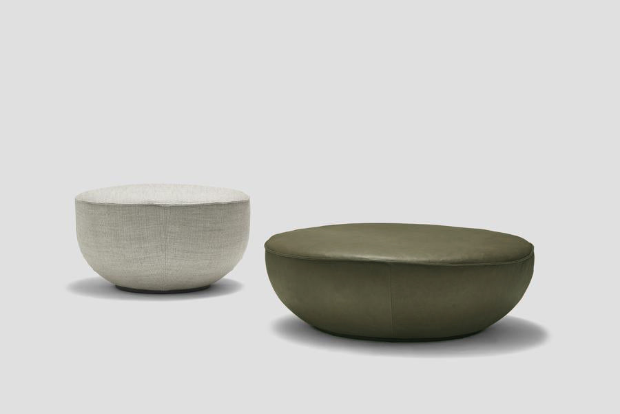 Two round Fable Ottomans by Wooden Stories are shown on a plain background: a smaller one in light gray fabric and a larger Fable Ottoman | Leather in olive green—both perfect for extra seating.