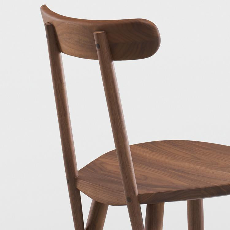 The Figura Dining Chair by Wooden Stories, shown from a rear side angle against a white background, features an espresso oak finish, curved backrest, angled legs, and minimalist design that reflects heritage woodworking craftsmanship.