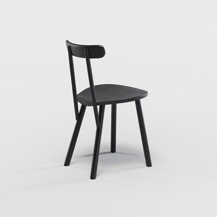 The Figura Dining Chair by Wooden Stories is crafted from black oak with three legs and a curved backrest, blending heritage woodworking with minimalist style. Shown on a plain white background, the chair is angled slightly left.