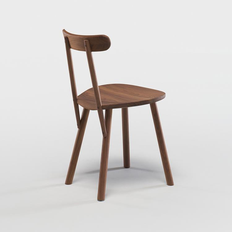 The Figura Dining Chair by Wooden Stories features a minimalist solid espresso oak design with a curved backrest and four angled legs, shown against a plain white background. Inspired by heritage woodworking.