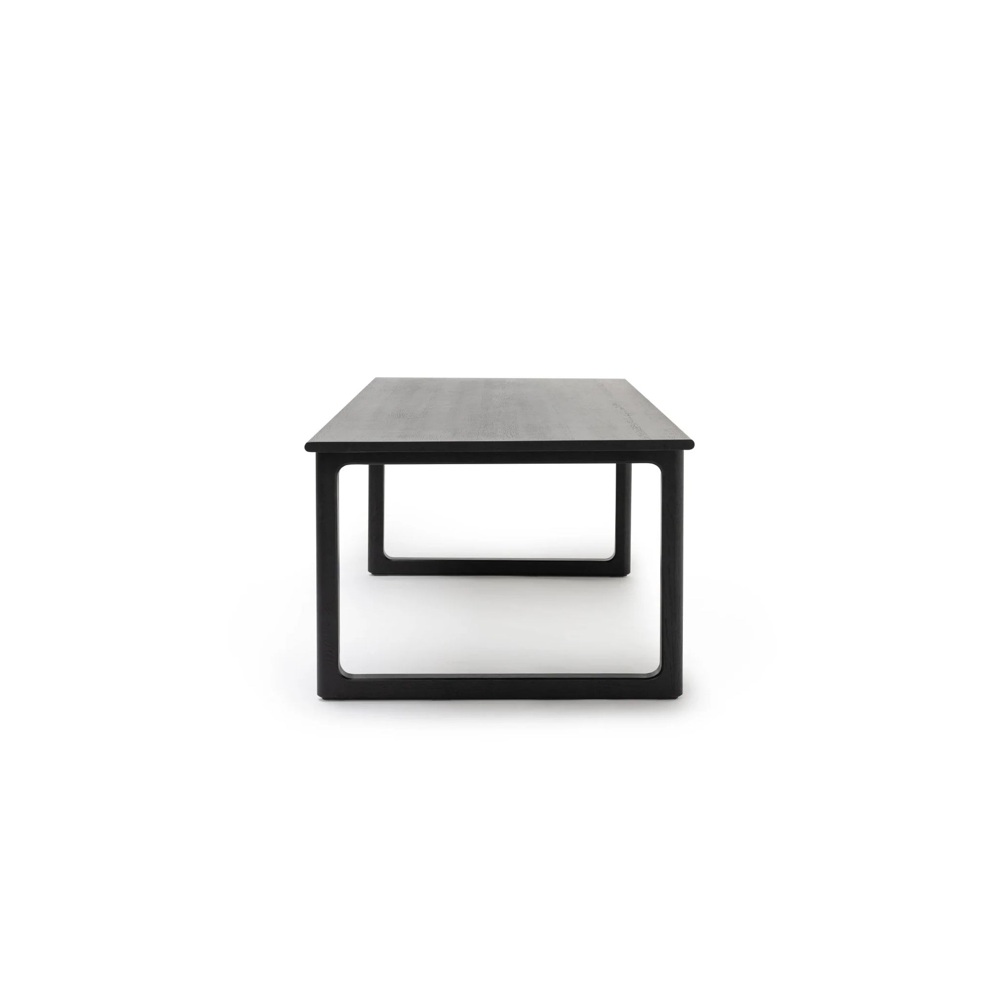 The Wooden Stories Hover Dining Table in Black Oak, featuring Danish-inspired lines, a flat top, and open square legs, is shown from the narrow end against a white background.