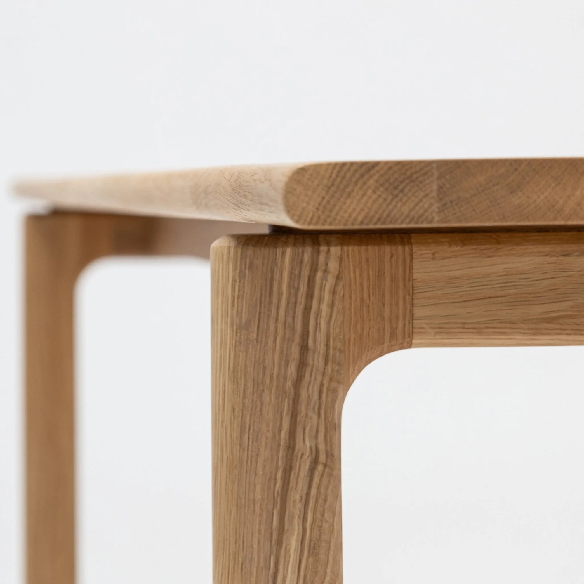 Close-up of the Hover Dining Table | Light Oak by Wooden Stories, highlighting its smooth, rounded corner, minimalist Danish design, and light oak grain against a plain white background.