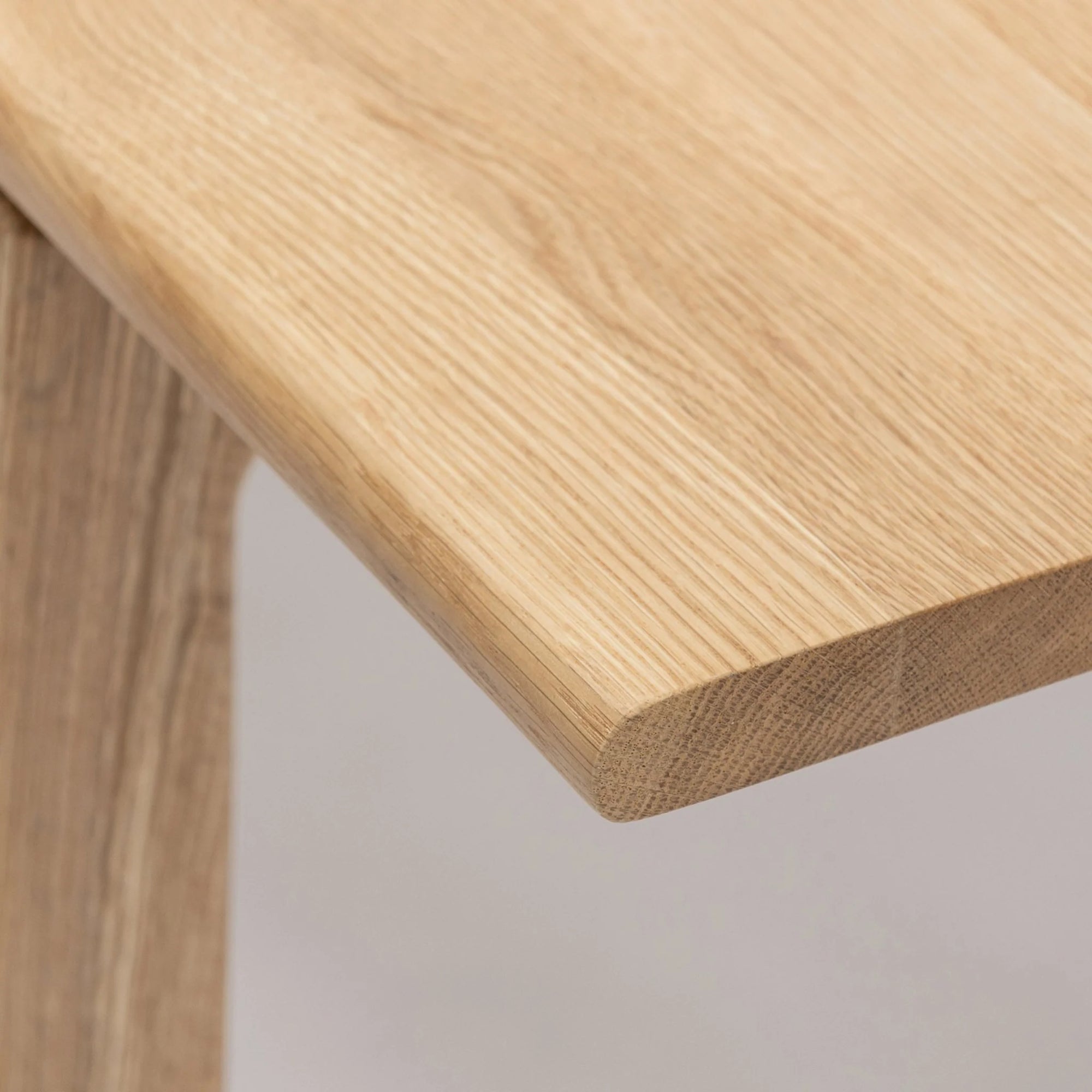 A close-up of Wooden Stories’ Hover Dining Table | Light Oak highlights its smooth, rounded corner and visible wood grain—classic Danish style that elevates any dining room against a simple, light backdrop.