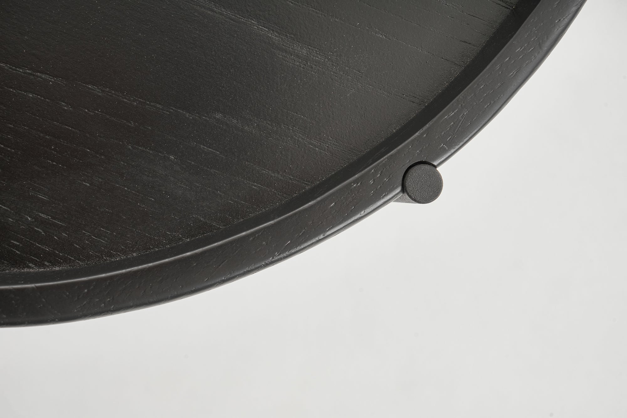 Close-up of the Humla Round Side Table by Wooden Stories, showing its dark wood edge with a raised rim and small cylindrical knob, crafted in Danish design style, set against a plain white background.