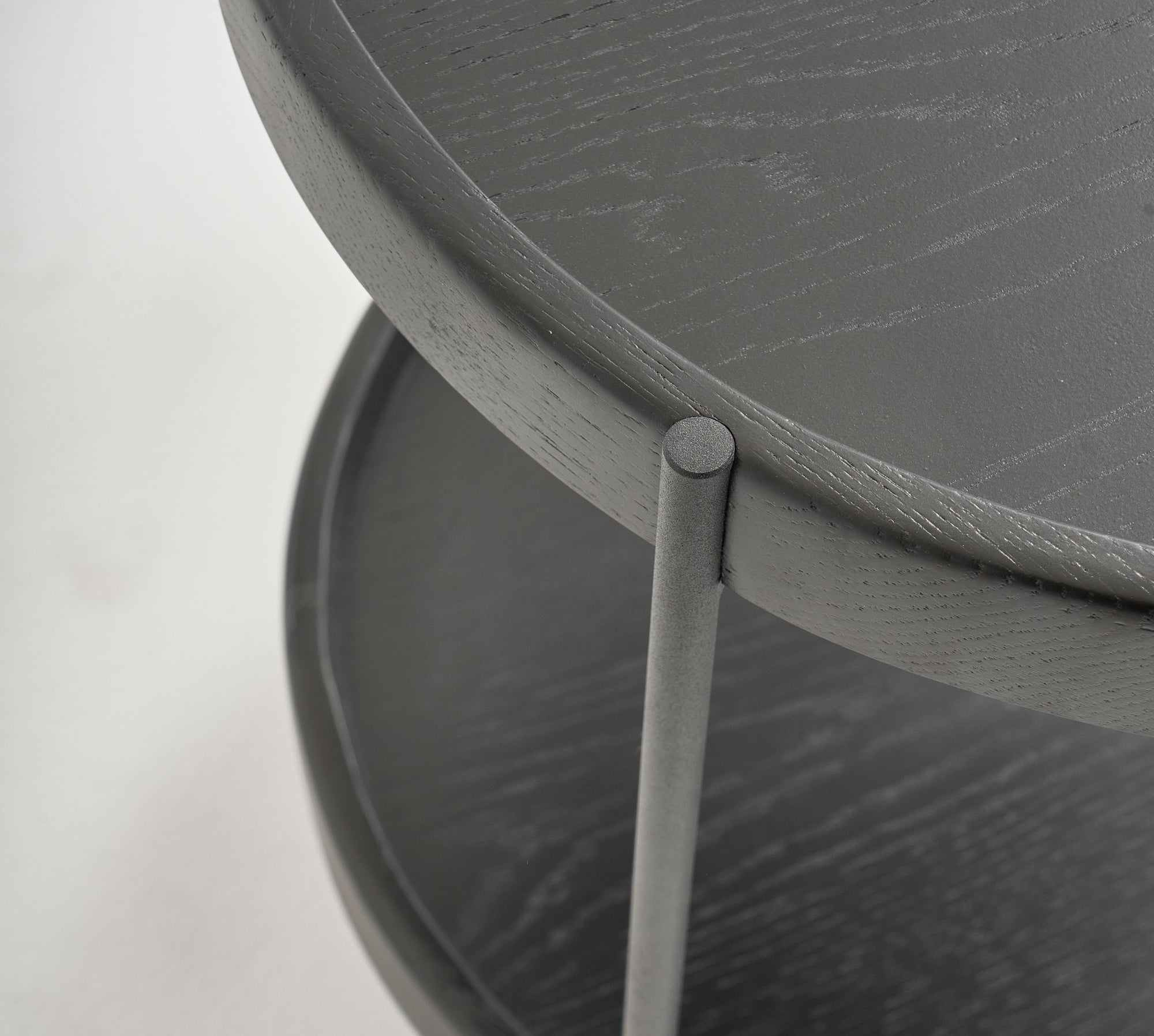 Close-up of the Humla Round Side Table by Wooden Stories, featuring Danish-inspired design with two tiers, a dark wood finish, and metal legs. Focus is on the edge and texture of the top and lower shelves.