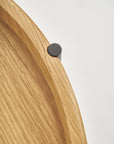 Close-up of the edge of the Wooden Stories Humla Round Side Table, inspired by Danish design, with a black circular metal detail on the light wood rim, shown against a plain white background.