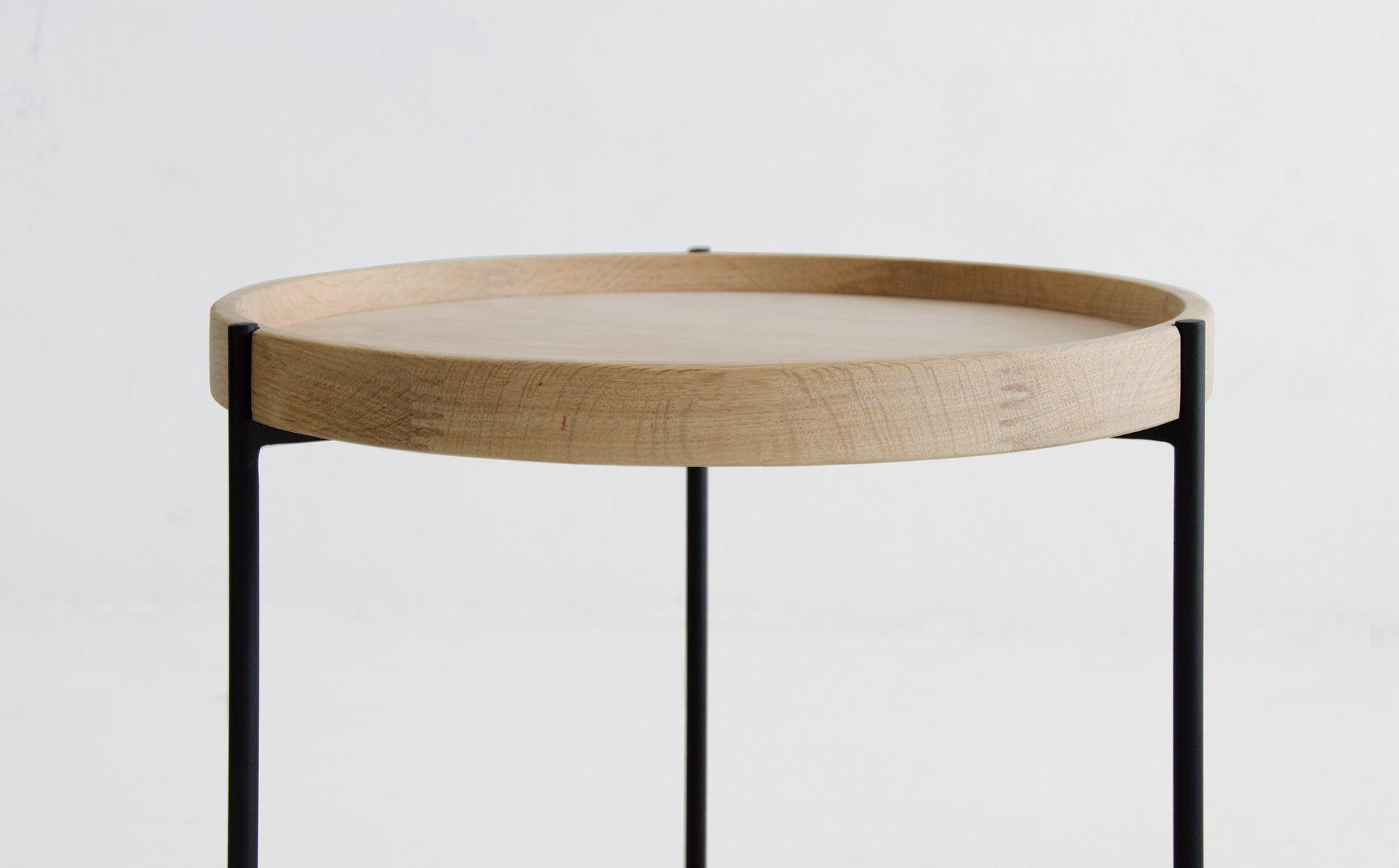 The Wooden Stories Humla End Table features Danish-inspired design, a round wooden top with a raised edge, thin black metal legs, and echoes the style of classic Hans Bolling Tray Tables, shown on a plain white background.