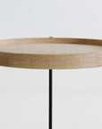 The Humla Round Side Table by Wooden Stories features a Danish-inspired wooden tray top with a raised edge and three slim black metal legs, set against a plain white background.