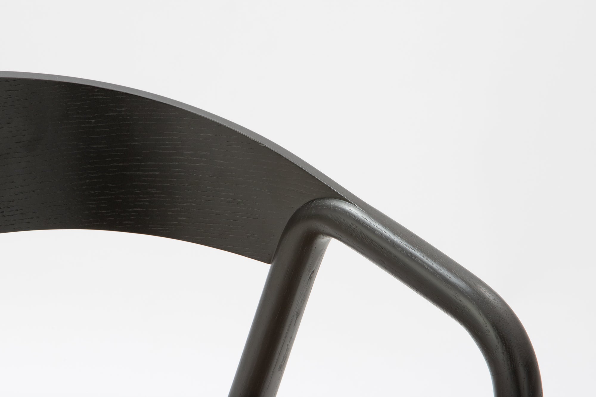 Close-up of the Inlay Dining Chair by Wooden Stories, showcasing black oak, a curved plywood backrest, solid wood arms, and a leather seat against a plain white background.