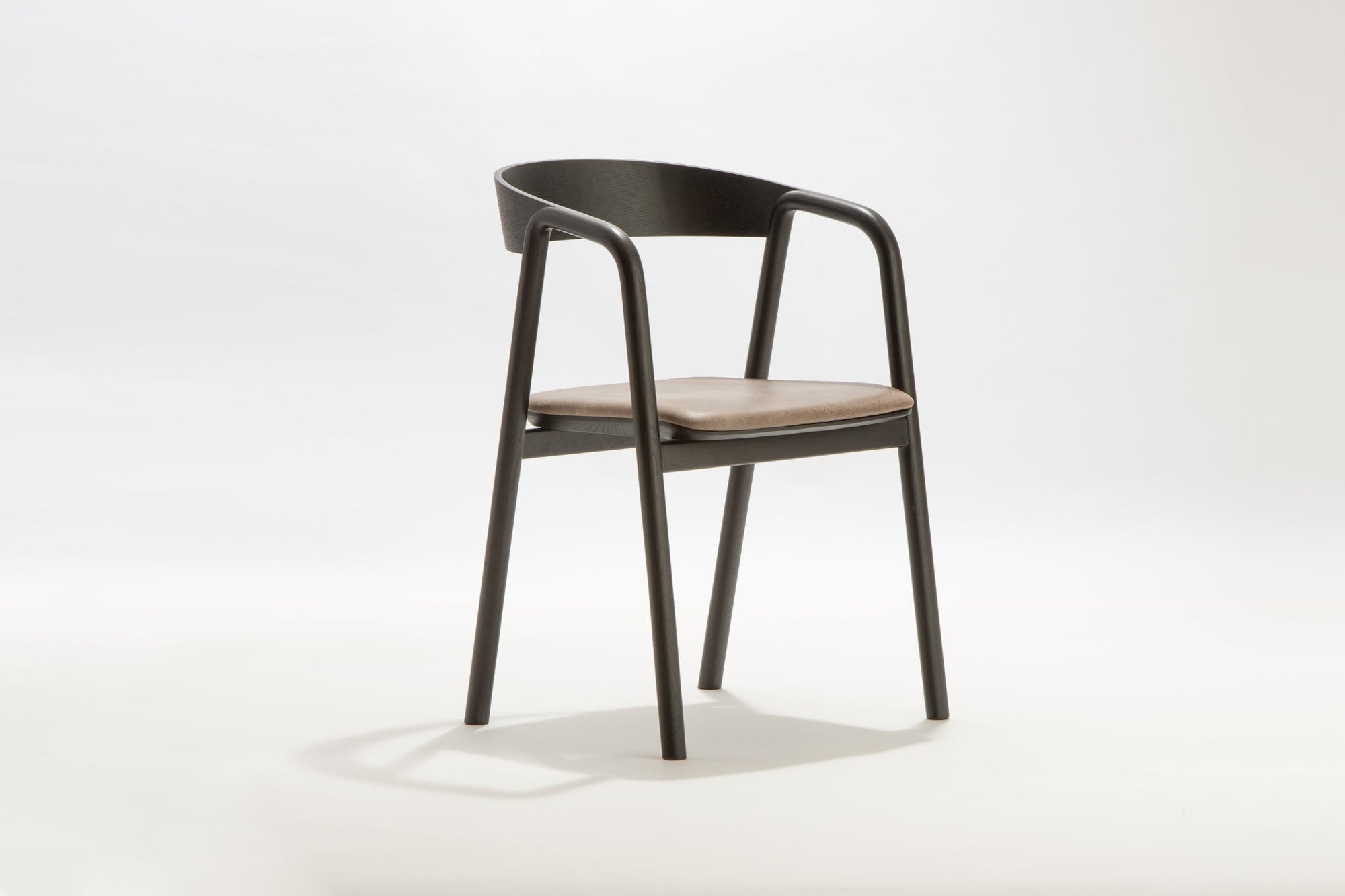 The Inlay Dining Chair by Wooden Stories features a black oak frame, leather seat, and curved backrest. Shown on a plain white background, it blends modern design with comfort.
