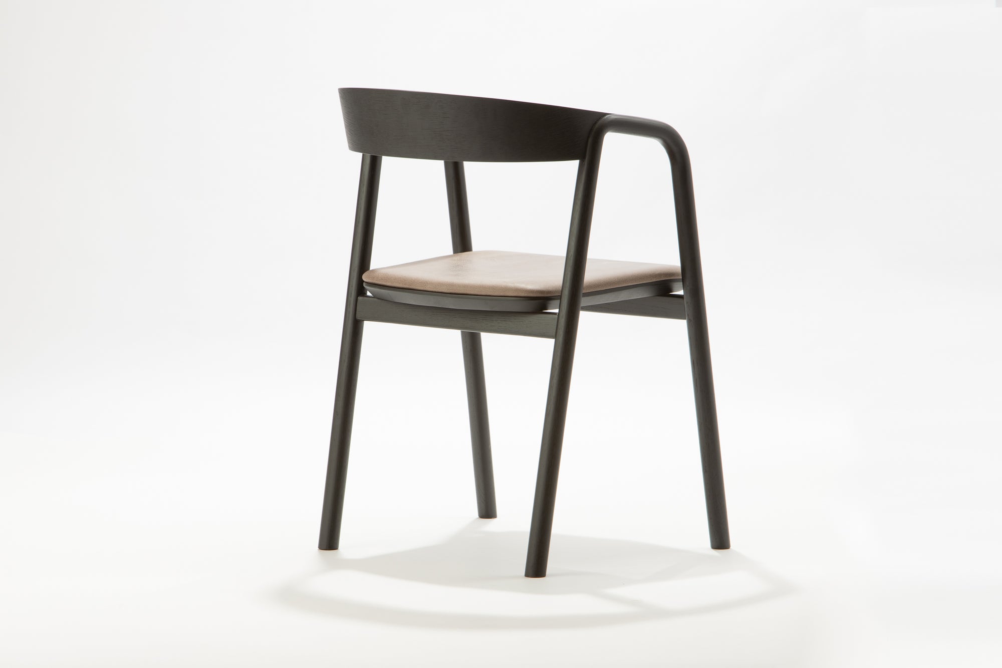 The Wooden Stories Inlay Dining Chair in Black Oak and Leather features a plywood backrest, solid wood arms, and a light leather cushioned seat, showcased against a plain white background.
