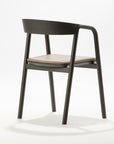 The Wooden Stories Inlay Dining Chair in Black Oak and Leather features a plywood backrest, solid wood arms, and a light leather cushioned seat, showcased against a plain white background.